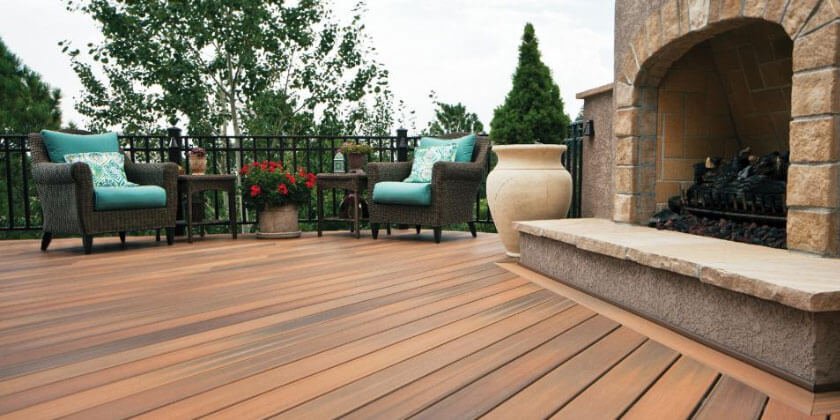 Outdoor patio with a fireplace and seating area featuring teal cushions, designed by a top Boston deck builder.