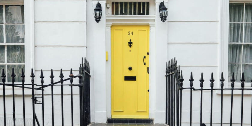 A bright yellow door numbered 34 on a white-facaded building with black railings, matching wall lanterns, and renovated by a general contractor.